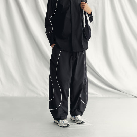 AEREN PANTS | BLACK with wide legs, elastic waistband, drawstring hem, side pockets, and a metallic line design.